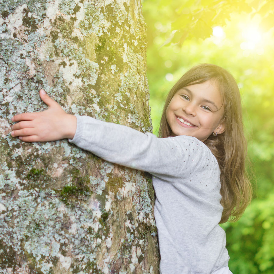Lächelndes Mädchen umarmt glücklich einen Baum